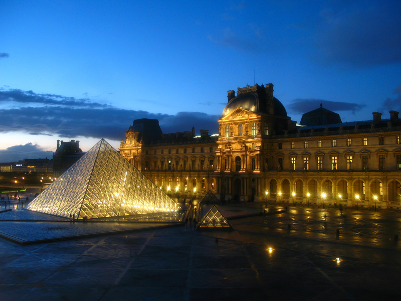 The most visited museum in the world, Louvre in Paris, France magnificent illuminated at twilight, as seen from the Denon Wing. Its history goes back 800 years of continuous transformations from fortress to palace and today museum.  Mona Lisa by Leonardo Da Vinci is only one of the works of art exhibited today inside. Image taken through an old thick and irregular glass, and lights have a special glow due to this fact.