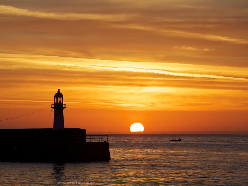 silloutte of the harbour lighthouse in St Ives, Cornwall with the golden sun rising over the Atlantic ocean